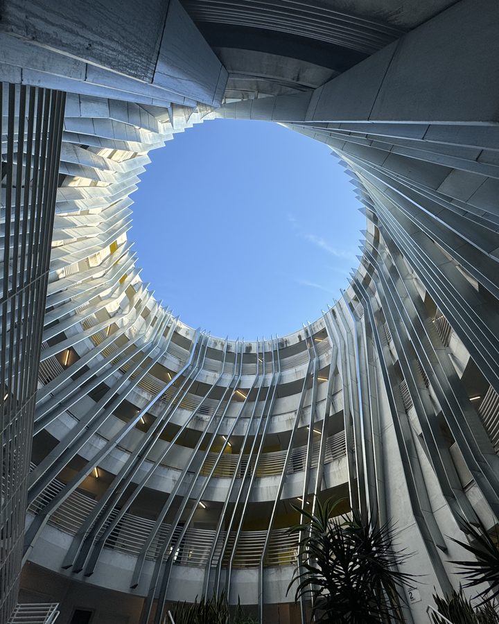 Looking straight up through a round open-air atrium ringed by white railings and balconies to a blue sky